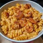 Assiette de pâtes crémeuses avec morceaux de poulet doré et crevettes, nappées d’une sauce épicée au fromage, texture onctueuse et appétissante.