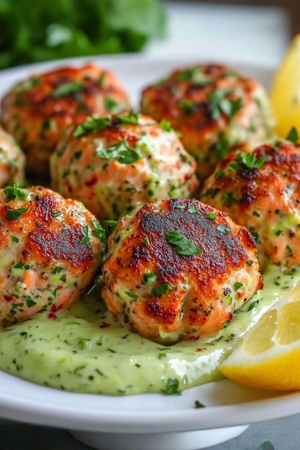 Boulettes de saumon dorées au four servies avec une crème d’avocat onctueuse et citronnée, dressées avec des herbes fraîches dans une assiette moderne.