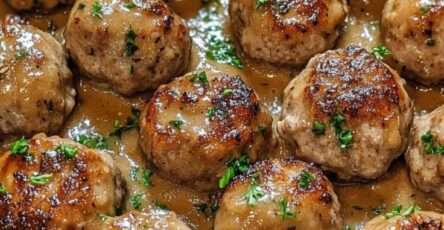 Boulettes de viande dorées nappées d’une sauce brune onctueuse, servies chaudes avec du persil frais dans une assiette généreuse.