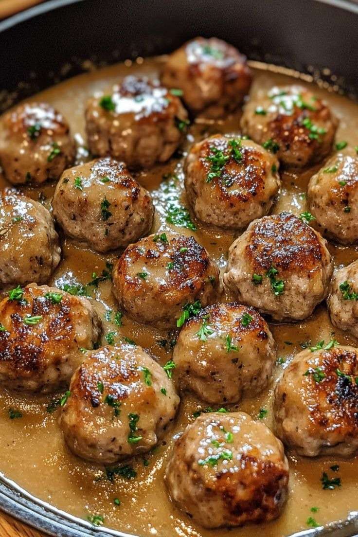Boulettes de viande dorées nappées d’une sauce brune onctueuse, servies chaudes avec du persil frais dans une assiette généreuse.