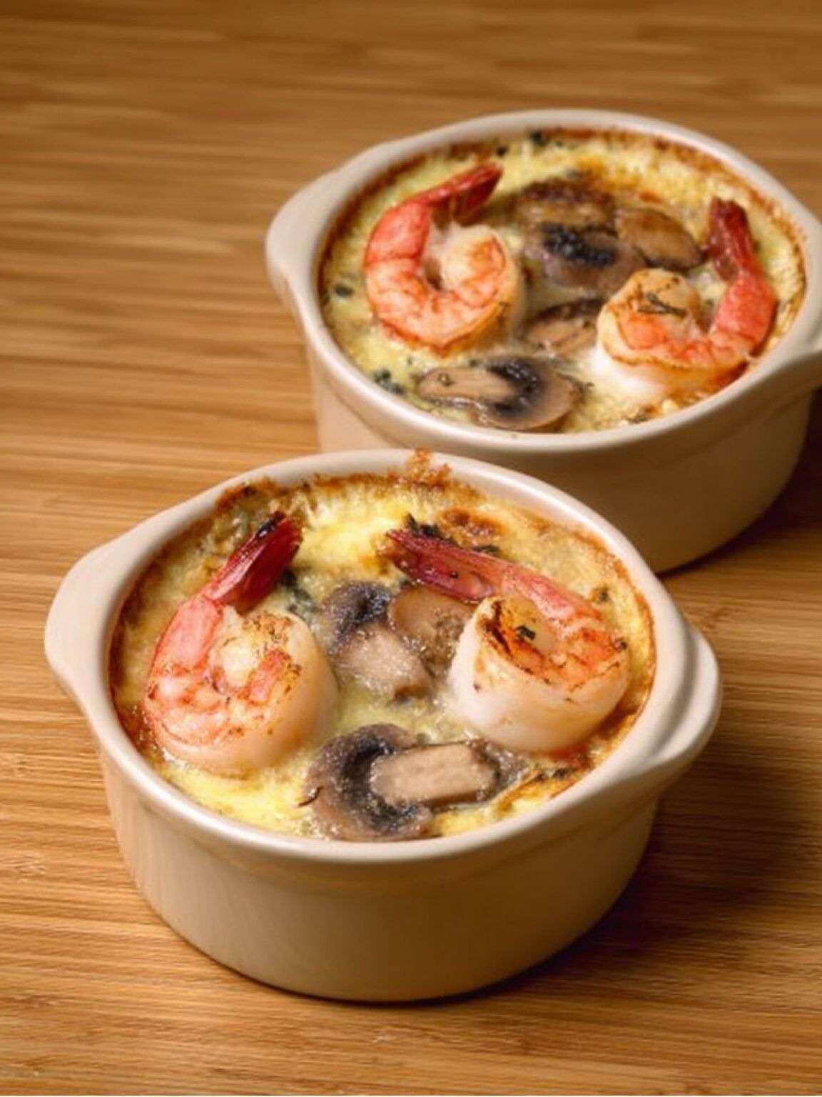 Cassolette de Saint-Jacques, crevettes et champignons dans une sauce crémeuse gratinée, servie bien chaude avec persil frais et croûte dorée.