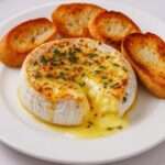 Camembert fondant entier fondu au four avec thym et ail, texture coulante, servi dans sa boîte avec pain croustillant à tremper.