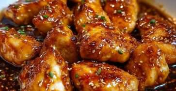 Morceaux de poulet teriyaki brillante, parsemés de sésame et ciboulette, servis avec du riz dans une assiette.