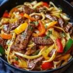 Nouilles sautées au bœuf avec poivrons colorés, oignon et herbes fraîches, servies chaudes dans un wok.