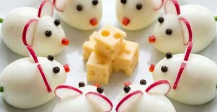 Œufs souris durs décorés en petites souris avec oreilles en radis, yeux en poivre, nez en carotte et queue en ciboulette, présentés avec cubes de fromage.