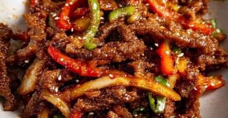 Lamelles de bœuf croustillant enrobées de sauce brillante sucrée salée avec poivrons rouges et verts, servies dans un wok fumant.