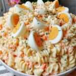 Salade de pâtes fusilli avec surimi, œufs durs, carottes et sauce crémeuse, garnie d’herbes fraîches dans un saladier.