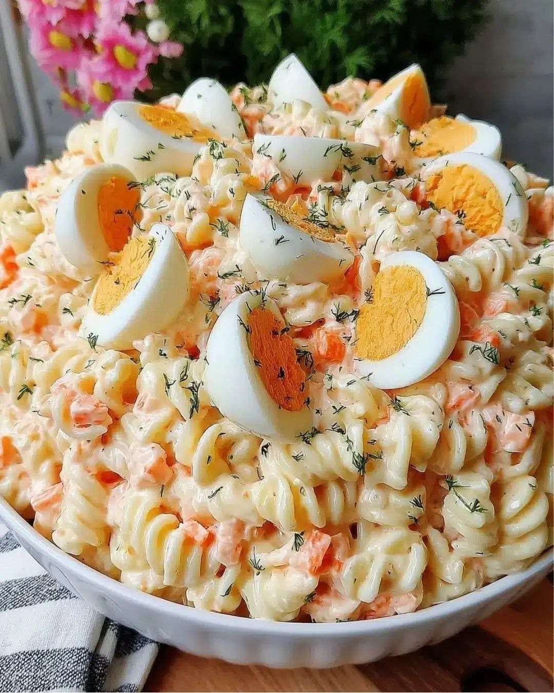 Salade de pâtes fusilli avec surimi, œufs durs, carottes et sauce crémeuse, garnie d’herbes fraîches dans un saladier.
