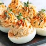 Œufs mimosa garnis de crème onctueuse au fromage frais, saupoudrés de paprika et décorés de thym frais sur un plat.