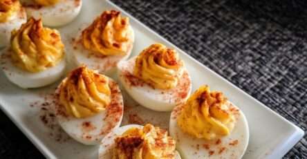 Œufs mimosa garnis d’une crème onctueuse au paprika fumé, légèrement pimentée, décorés d’herbes fraîches et présentés sur un plateau.