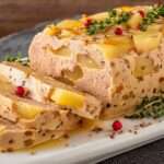 Terrine de foie gras aux poires maison, tranches fondantes avec morceaux de poires visibles, servies avec pain grillé sur une assiette élégante.