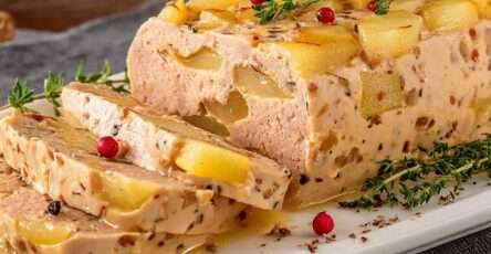 Terrine de foie gras aux poires maison, tranches fondantes avec morceaux de poires visibles, servies avec pain grillé sur une assiette élégante.