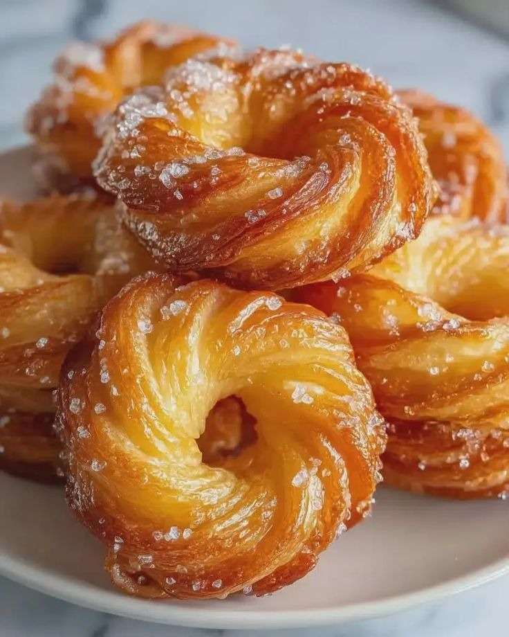 Assiette de crullers français au four dorés et légèrement croustillants, saupoudrés de sucre glace, avec une texture moelleuse à l’intérieur et une forme d’anneau régulière.