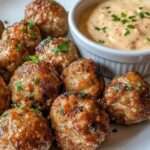 Assiette de boulettes de viande dorées et légèrement croustillantes, servies chaudes avec une sauce crémeuse à la moutarde et au miel dans un petit bol.