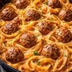 Assiette de pâtes crémeuses nappées de sauce tomate et crème, accompagnées de boulettes de viande dorées, parmesan râpé et persil frais.