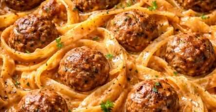 Assiette de pâtes crémeuses nappées de sauce tomate et crème, accompagnées de boulettes de viande dorées, parmesan râpé et persil frais.
