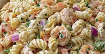 Salade de pâtes froides aux crevettes, petits pois, carottes râpées et oignon rouge, enrobée d’une sauce crémeuse, servie dans un grand saladier.