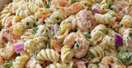 Salade de pâtes froides aux crevettes, petits pois, carottes râpées et oignon rouge, enrobée d’une sauce crémeuse, servie dans un grand saladier.