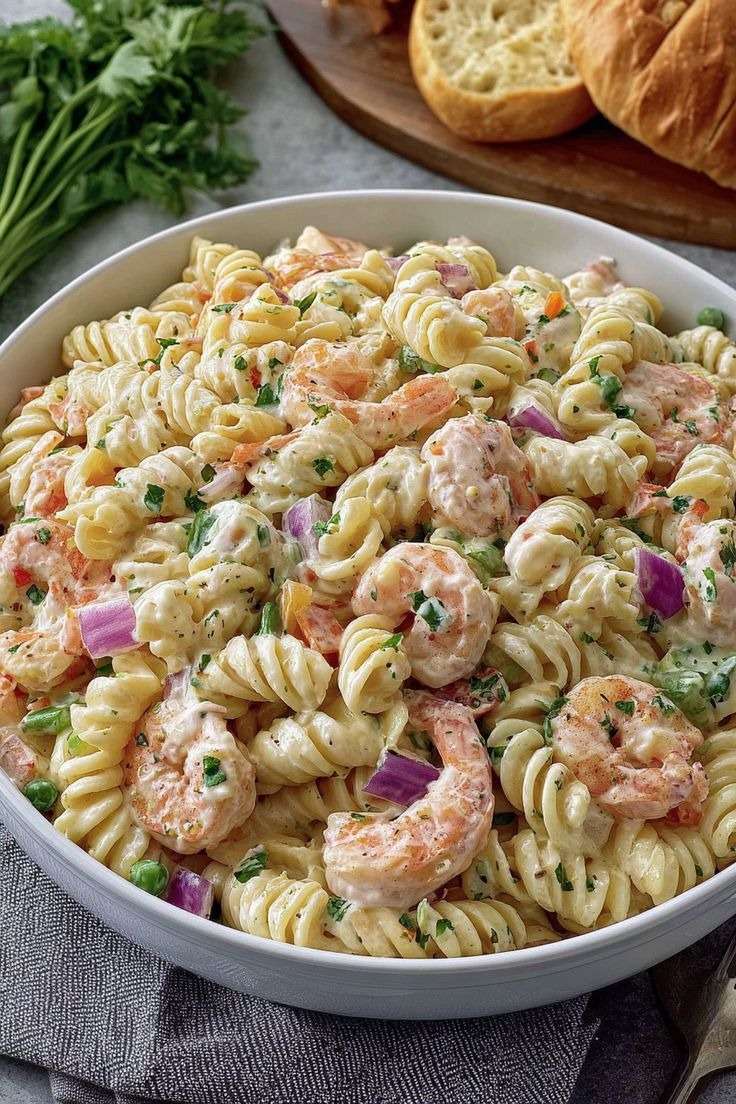 Salade de pâtes froides aux crevettes, petits pois, carottes râpées et oignon rouge, enrobée d’une sauce crémeuse, servie dans un grand saladier.