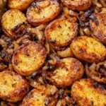 Pommes de terre rôties dorées au four avec des oignons caramélisés fondants, assaisonnées au paprika et au thym, servies dans un plat rustique.