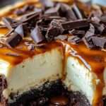 Cheesecake brownie au chocolat avec couche crémeuse et nappage caramel beurre salé coulant, décoré de morceaux de chocolat noir.