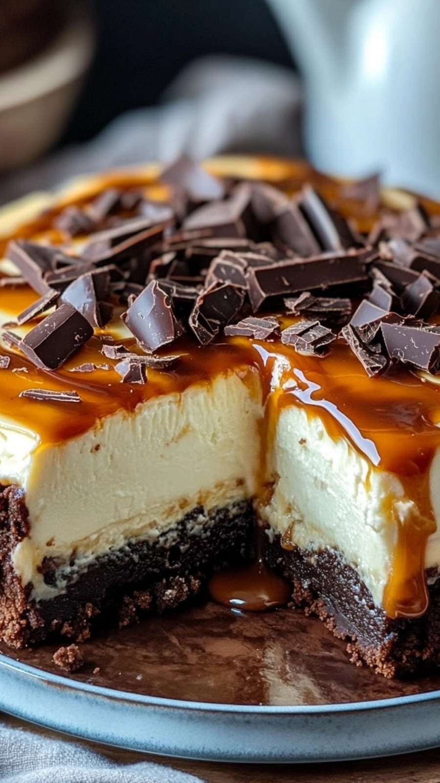 Cheesecake brownie au chocolat avec couche crémeuse et nappage caramel beurre salé coulant, décoré de morceaux de chocolat noir.