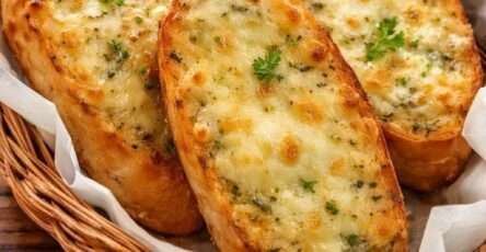 Pain à l’ail gratiné au fromage servi chaud sur une planche en bois, avec croûte dorée et croustillante, fromage fondu, persil frais et texture moelleuse à l’intérieur.