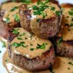 Médaillons de bœuf nappés de sauce crémeuse dans une assiette élégante, viande saisie et juteuse, garnie de persil frais avec une texture fondante.