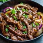 Assiette de sauté de bœuf aux oignons à la chinoise avec lamelles de viande brillantes, oignons légèrement caramélisés et sauce nappante, servie avec du riz blanc.