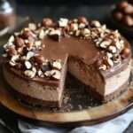 Cheesecake sans cuisson au Nutella et noisette avec base biscuitée, garniture crémeuse lisse et décor de noisettes, chocolat et filet de Nutella.