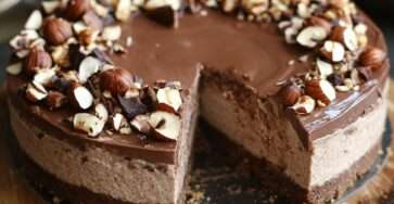 Cheesecake sans cuisson au Nutella et noisette avec base biscuitée, garniture crémeuse lisse et décor de noisettes, chocolat et filet de Nutella.