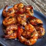 Crevettes sautées brillantes nappées de sauce miel-soja avec ail doré et herbes fraîches, servies dans une poêle avec une finition brillante.