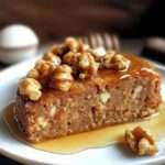 Gâteau aux noix et au miel doré, texture moelleuse avec morceaux de noix visibles, présenté en tranches sur un plat rustique.