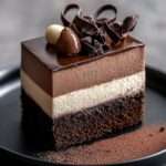 Entremets trois chocolats avec couches distinctes noir, lait et blanc, recouvert d’un glaçage brillant et décoré de copeaux de chocolat.