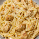 Assiette de pâtes crémeuses au poulet, ail et parmesan, avec une sauce onctueuse, des morceaux de poulet dorés et du parmesan râpé.