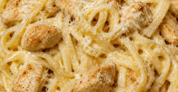 Assiette de pâtes crémeuses au poulet, ail et parmesan, avec une sauce onctueuse, des morceaux de poulet dorés et du parmesan râpé.