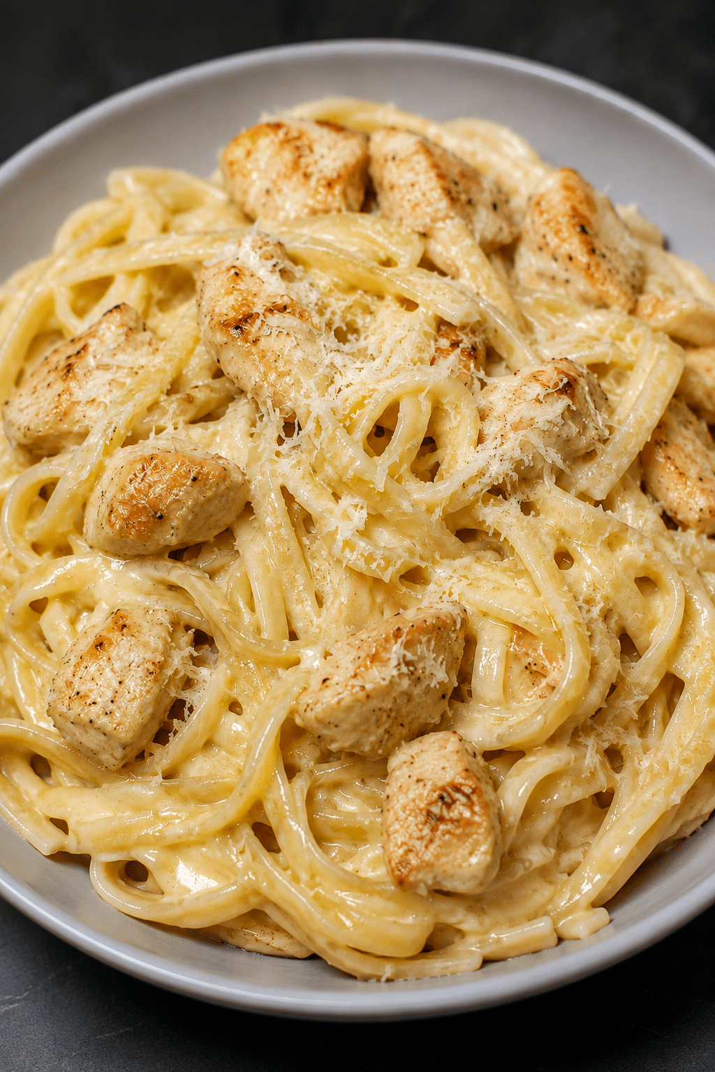 Assiette de pâtes crémeuses au poulet, ail et parmesan, avec une sauce onctueuse, des morceaux de poulet dorés et du parmesan râpé.