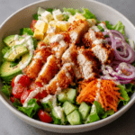 Salade complète au poulet croustillant avec salade verte, avocat, tomates, concombre, carotte râpée, oignon rouge et sauce crémeuse au yaourt.