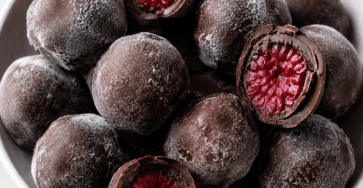 Bouchées glacées aux framboises enrobées de chocolat noir, avec une coque croquante et un cœur fruité, servies sur du papier cuisson.