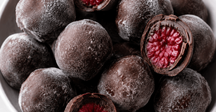 Bouchées glacées aux framboises enrobées de chocolat noir, avec une coque croquante et un cœur fruité, servies sur du papier cuisson.