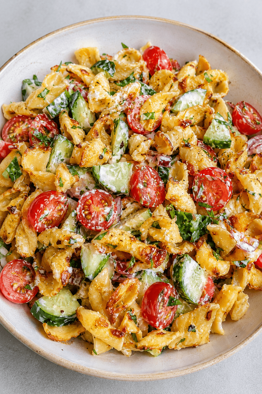 Salade de pâtes croustillantes façon TikTok servie dans un grand bol, avec tomates cerises, concombre, oignon rouge, herbes fraîches et sauce crémeuse au yaourt.