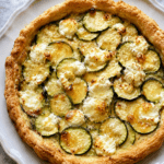 Tarte courgettes, chèvre et miel dorée au four, garnie de fines rondelles de courgettes, morceaux de fromage de chèvre fondant et filet de miel brillant.