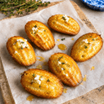 Madeleines salées au chèvre frais, miel et thym, dorées au four, servies tièdes avec un léger filet de miel brillant sur le dessus.