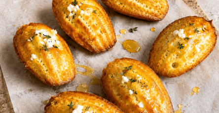Madeleines salées au chèvre frais, miel et thym, dorées au four, servies tièdes avec un léger filet de miel brillant sur le dessus.
