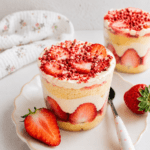 Cup façon fraisier servie dans un verre avec couches de génoise moelleuse, fraises fraîches coupées, crème vanille, chantilly et miettes de fraises séchées.