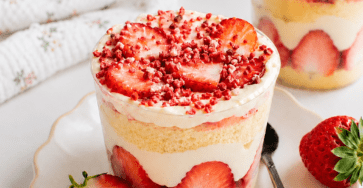 Cup façon fraisier servie dans un verre avec couches de génoise moelleuse, fraises fraîches coupées, crème vanille, chantilly et miettes de fraises séchées.