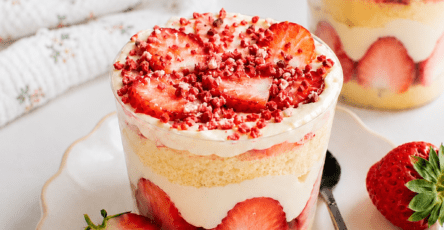 Cup façon fraisier servie dans un verre avec couches de génoise moelleuse, fraises fraîches coupées, crème vanille, chantilly et miettes de fraises séchées.