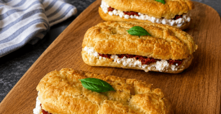 Éclair salé garni de crème de burrata à l’huile d’olive, de tomates confites rouges et de basilic frais, servi en bouchée apéritive.