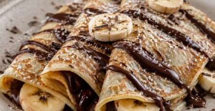 Crêpes fines et moelleuses garnies de chocolat fondant, de rondelles de banane fraîche et saupoudrées de sucre glace dans une assiette