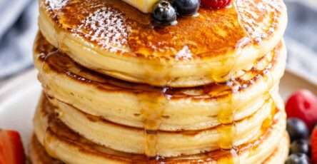 Pancakes moelleux empilés façon brunch, nappés de sirop d’érable, décorés de fruits rouges frais et légèrement saupoudrés de sucre glace.